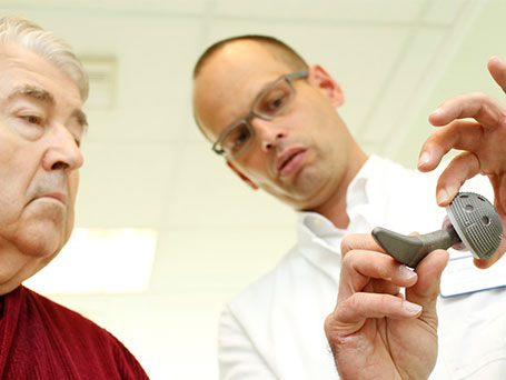 Bild Dr Schildknecht bei der Planung mit einem Patienten hält künstliches Hüftgelenk